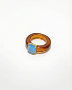 Ring with a blue gemstone and amber-colored band on a white background