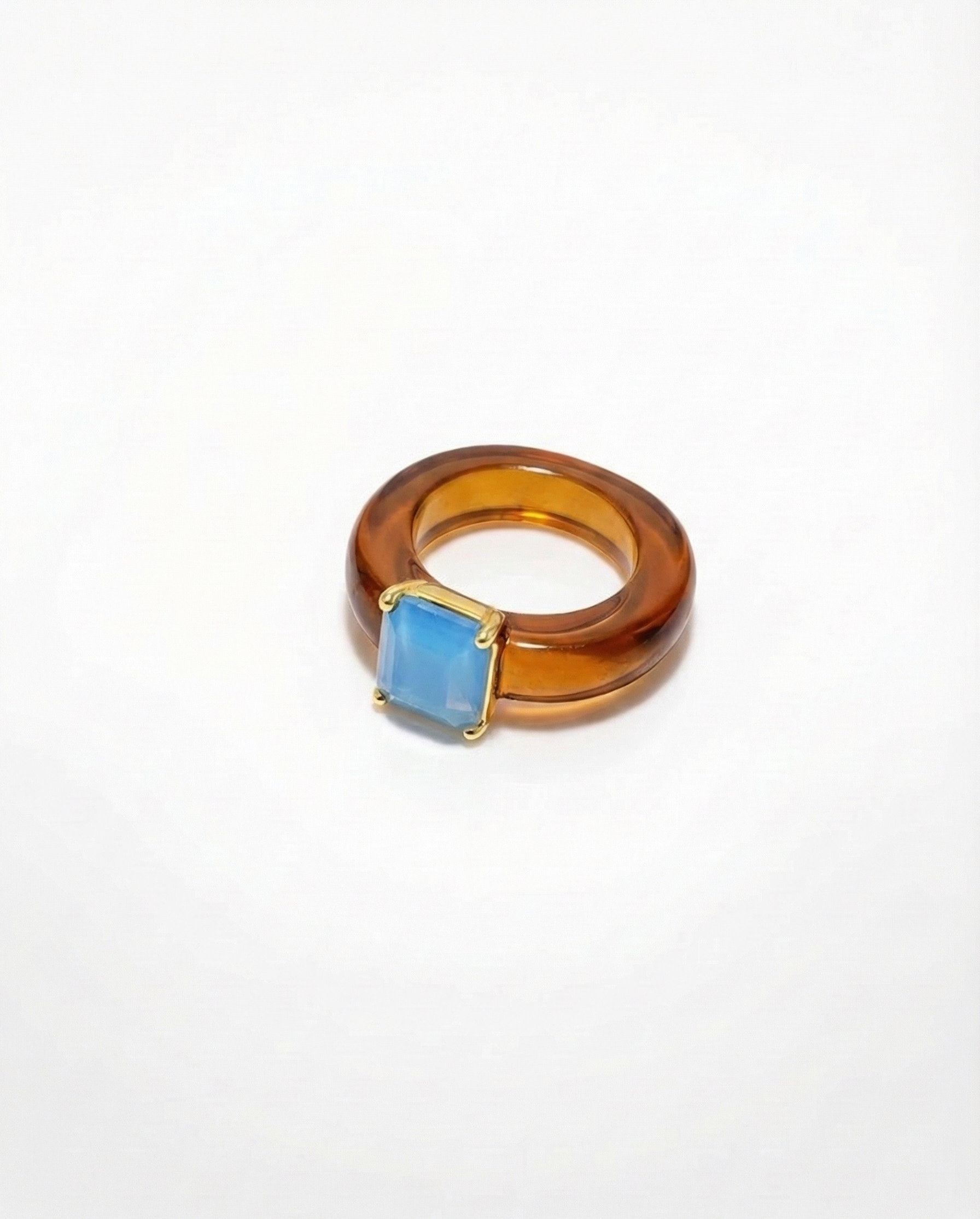 Ring with a blue gemstone and amber-colored band on a white background