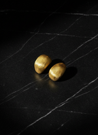 Two gold earrings on a black textured surface
