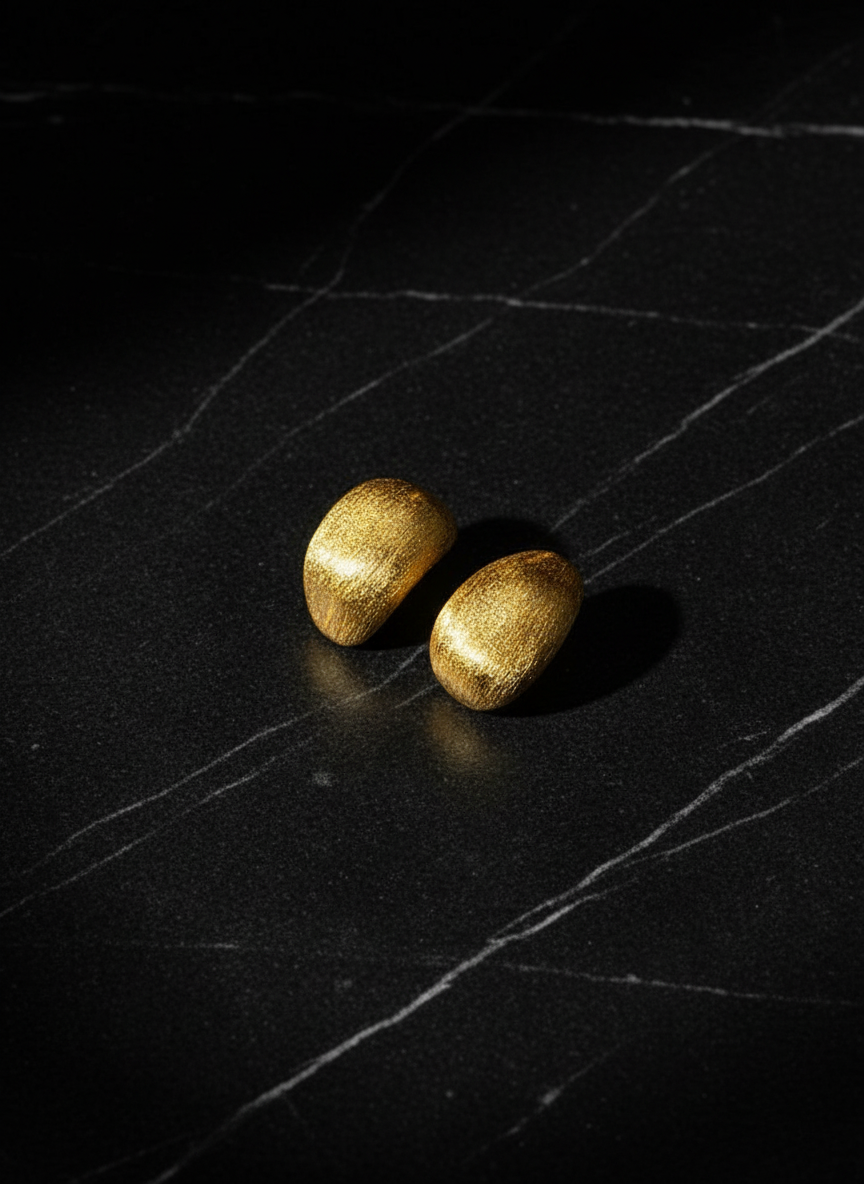 Two gold earrings on a black textured surface