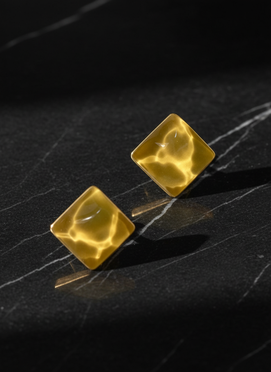 Gold square earrings on a dark textured surface by SFUMATO
