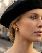 Woman wearing a black beret and gold earrings with a blurred outdoor background