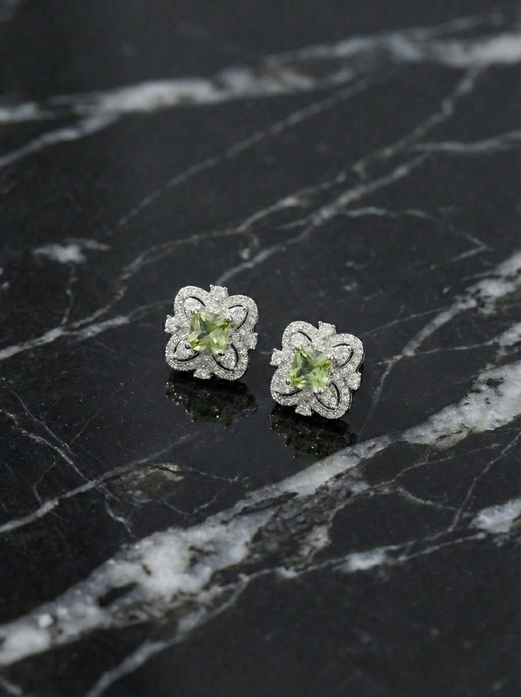 Pair of silver flower-shaped earrings with green gemstones on a black marble surface