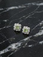 Pair of silver flower-shaped earrings with green gemstones on a black marble surface