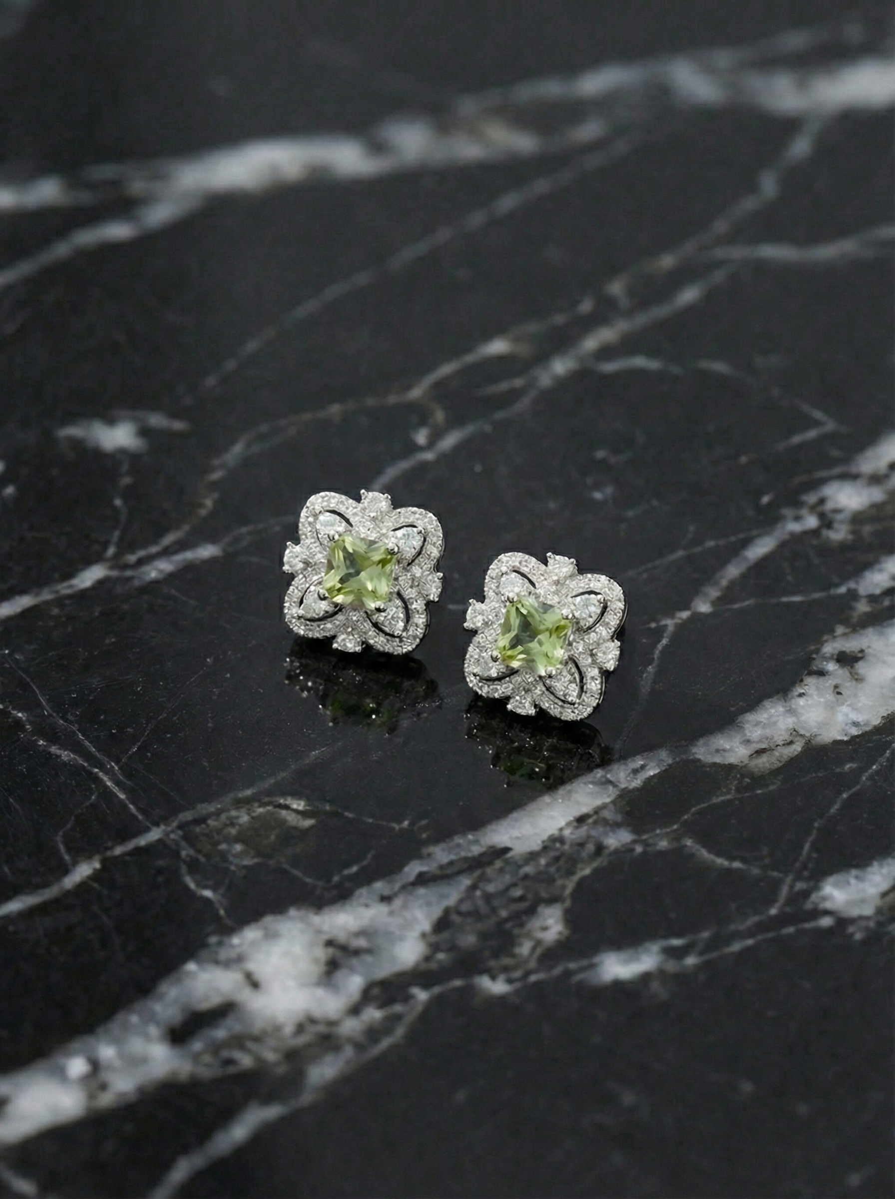 Pair of silver flower-shaped earrings with green gemstones on a black marble surface by SFUMATO