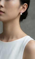 Close-up of a person wearing pearl earrings with a neutral background