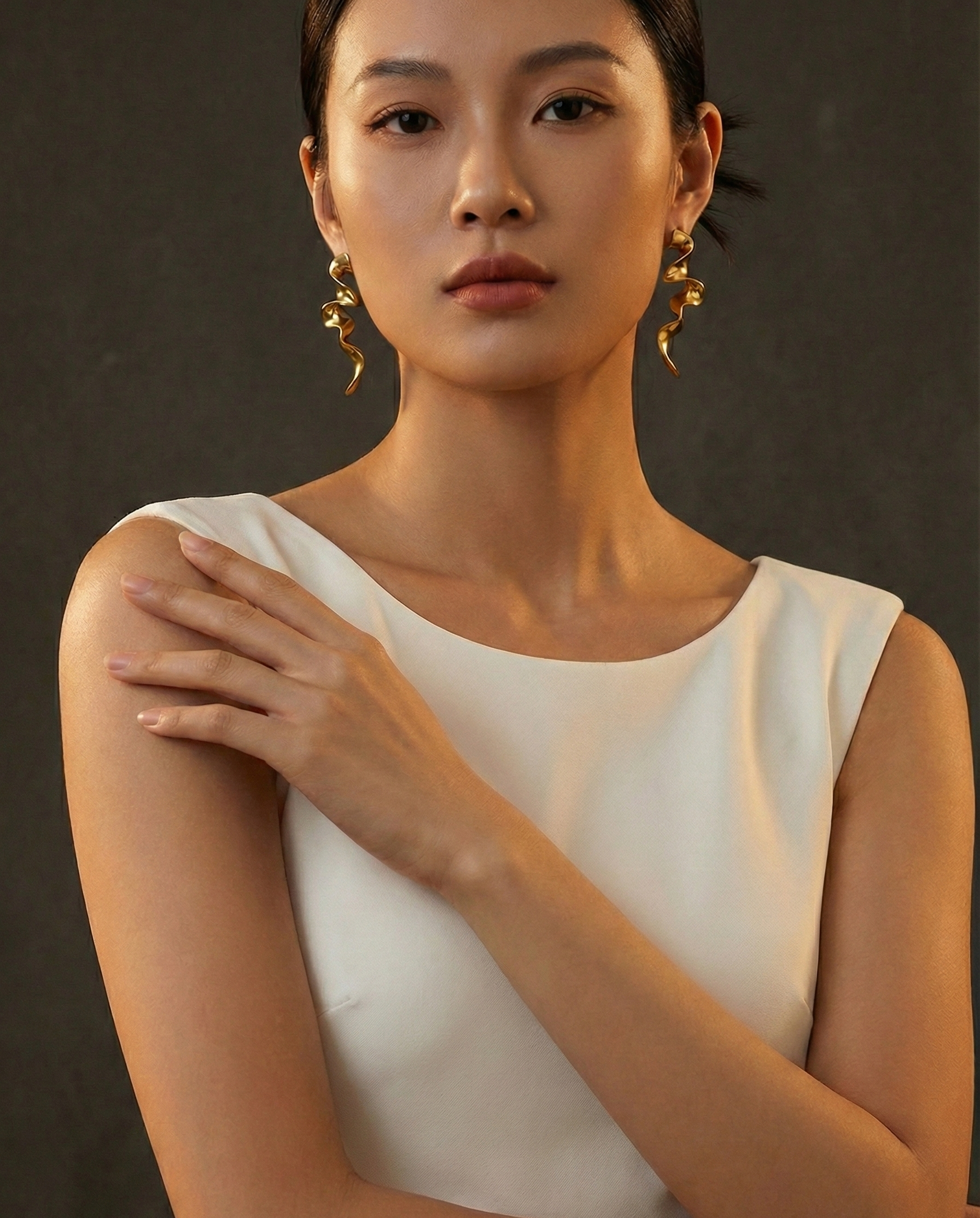 Woman wearing a white top with gold earrings against a dark background by SFUMATO