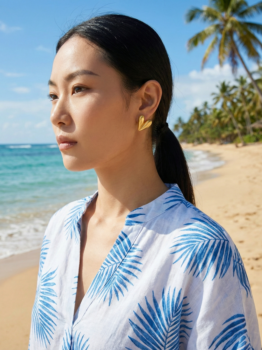 Woman wearing a blue and white patterned top on a beach with palm trees in the background