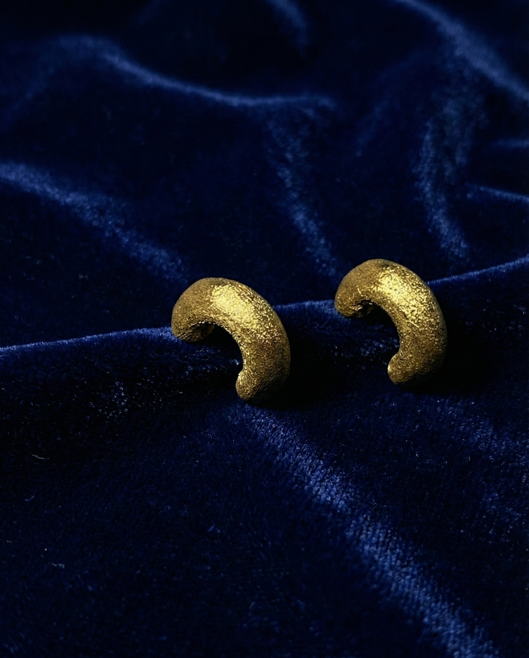 Gold crescent moon earrings on a blue velvet background by SFUMATO