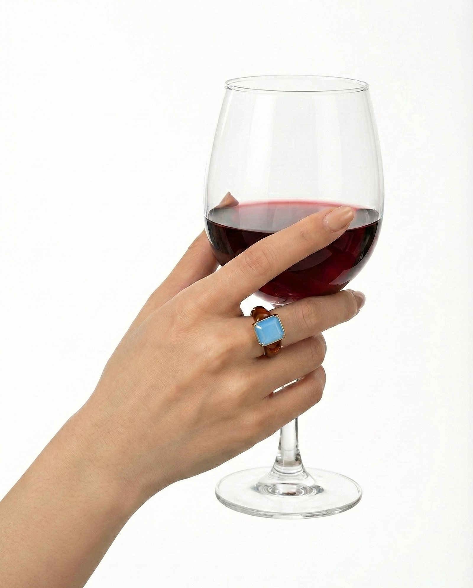 Hand holding a glass of red wine with a blue ring on a white background