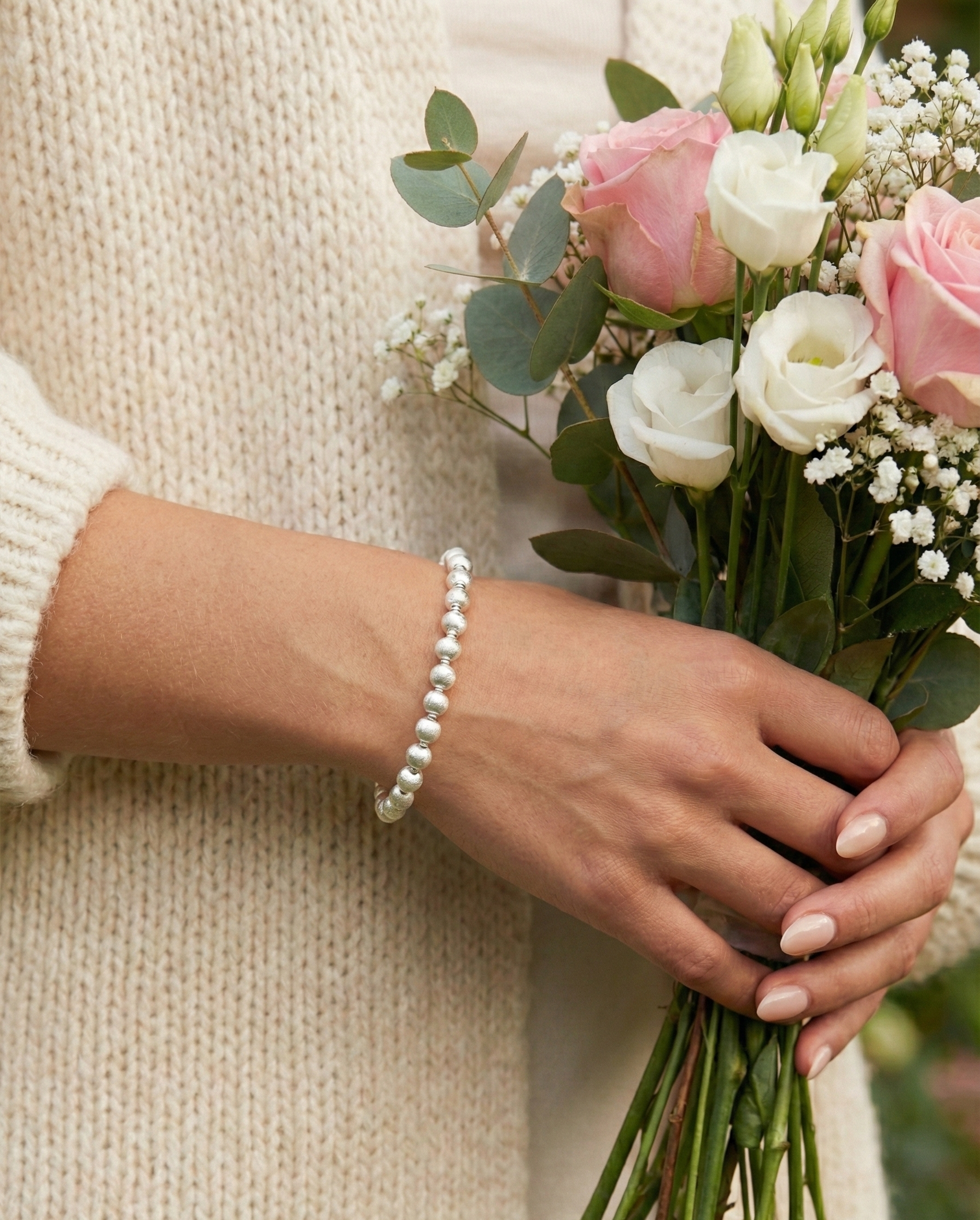 Person holding a bouquet of flowers wearing a pearl bracelet. by SFUMATO