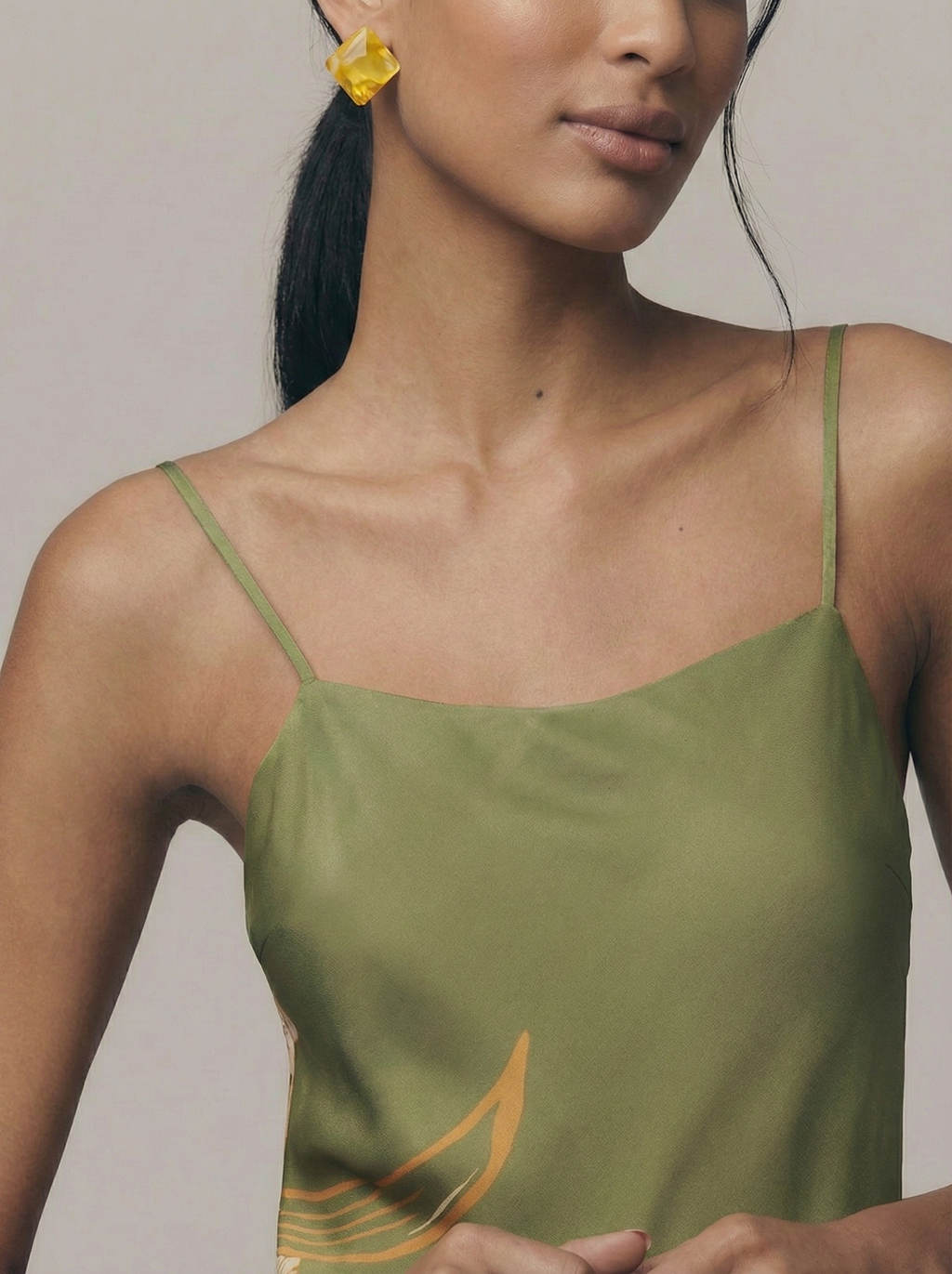 Woman wearing a green satin slip dress with thin straps against a neutral background