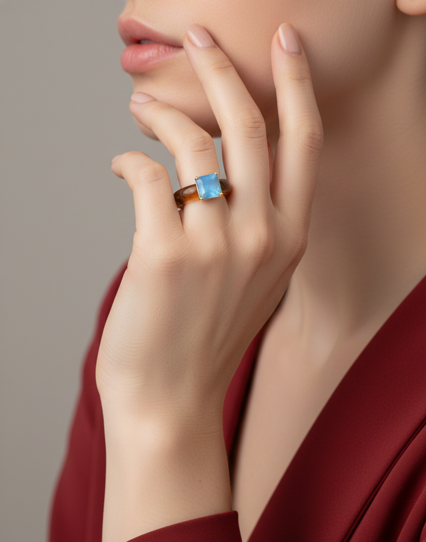 Close-up of a hand wearing a ring with a blue gemstone against a neutral background by SFUMATO