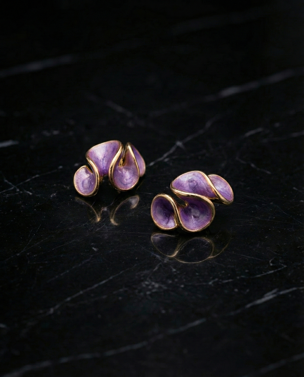 Pair of purple earrings with gold accents on a dark surface