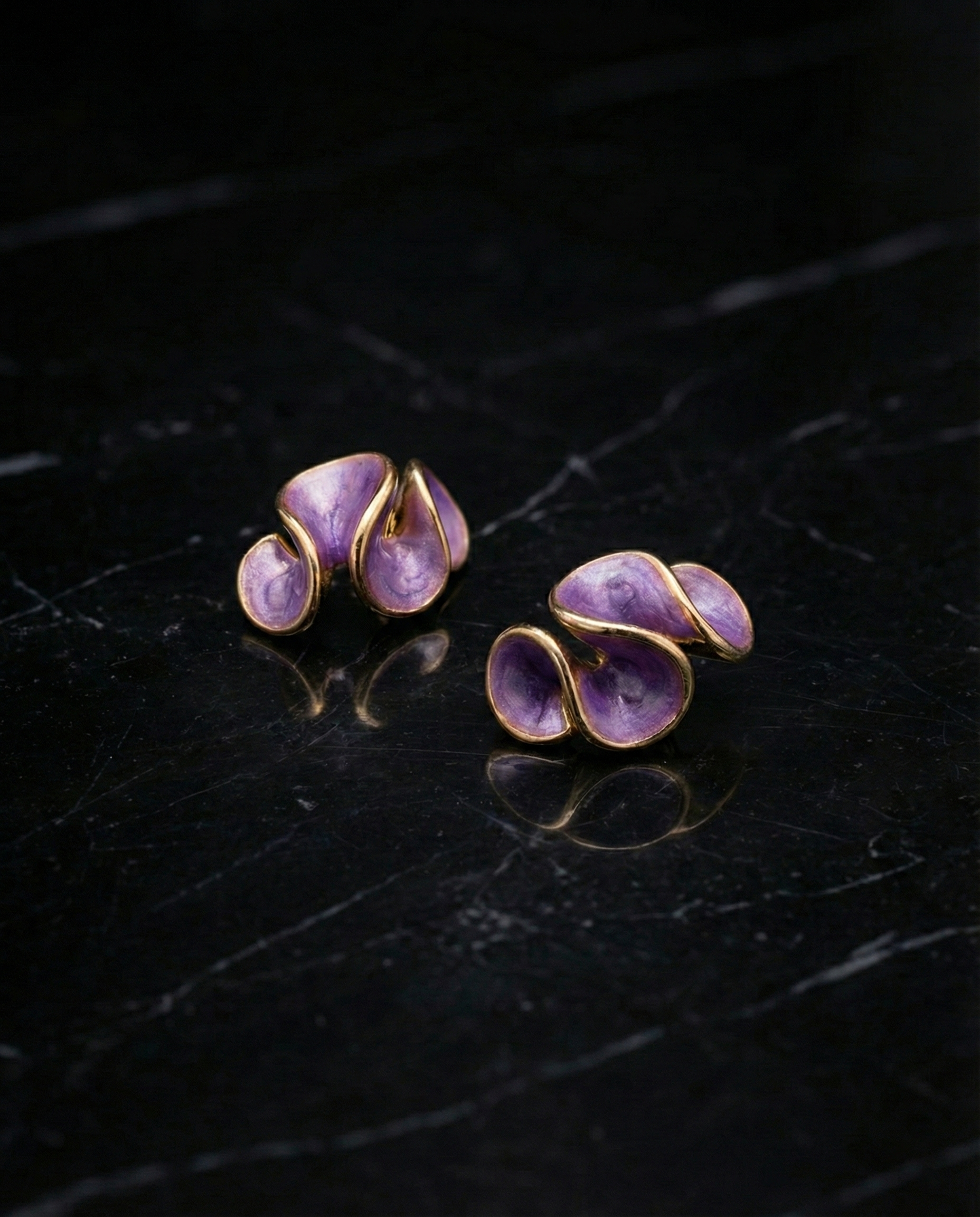 Pair of purple earrings with gold accents on a dark surface by SFUMATO